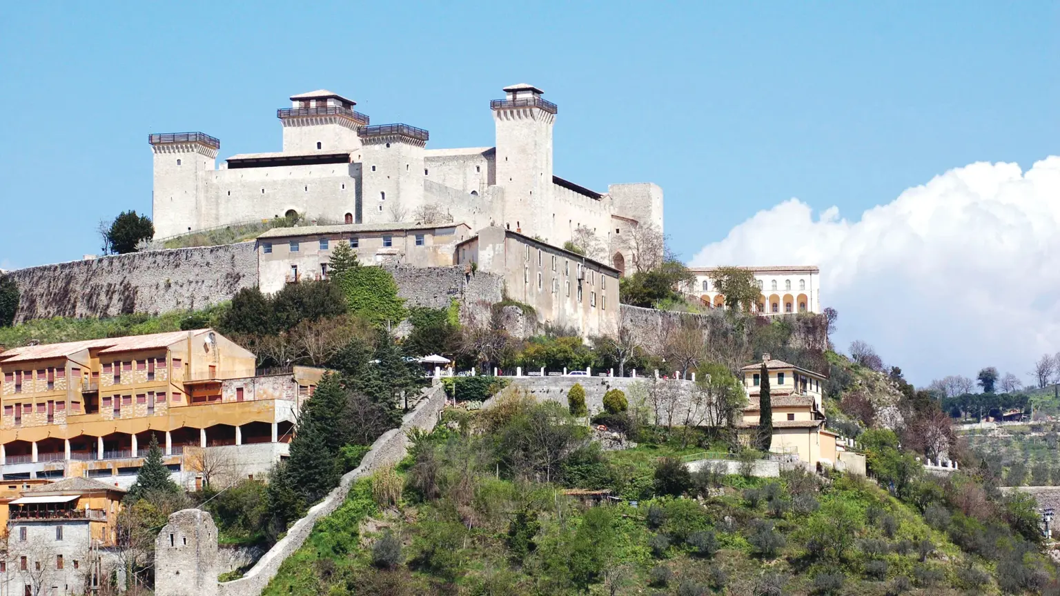 The white crenellated towers of the Rocca Albornoziana fortress on its hilltop above the ochre buildings of Spoleto