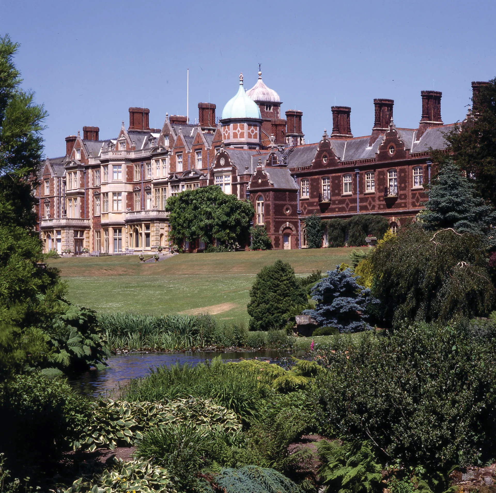 Jacobean-revival country house in red brick and pale stone, with ornate gables and chimneys, fronted by formal gardens