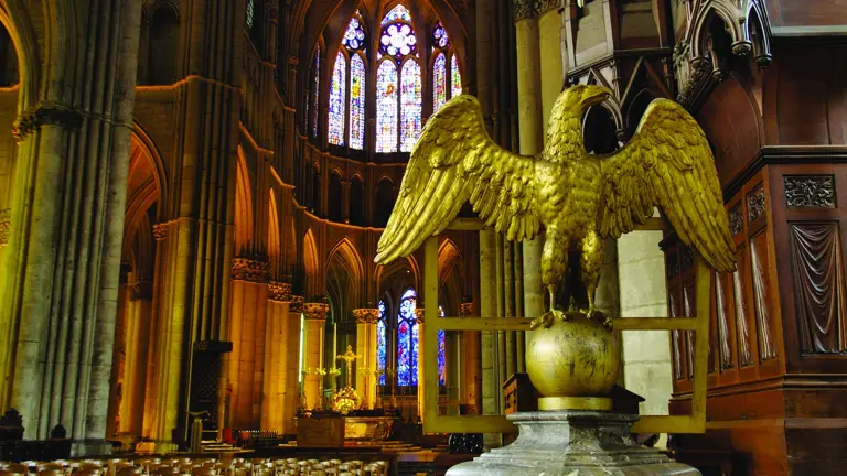 A soaring Gothic nave with a golden eagle lectern in the foreground and luminous stained-glass windows.