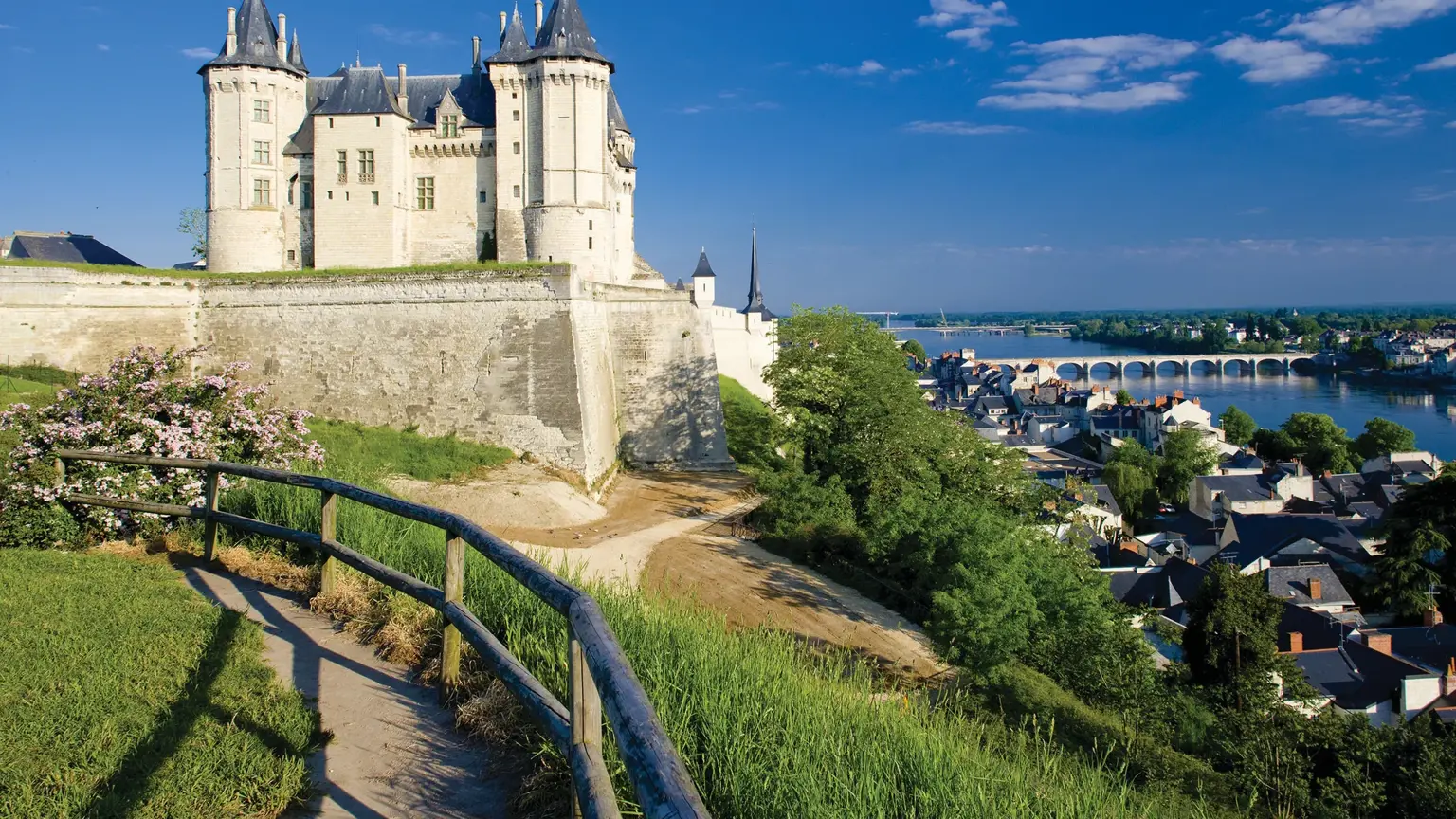 A fairytale white chateau on a green bluff above a riverside town and a long bridge.