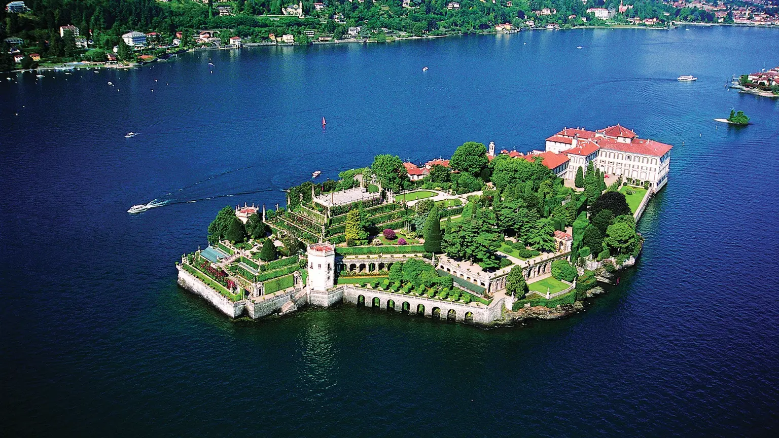 Aerial view of Isola Bella on Lake Maggiore, the Borromeo palace and its terraced baroque gardens filling the island, surrounded by deep blue water and wooded shores