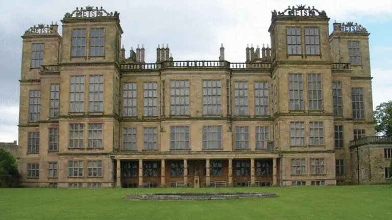 Grand Elizabethan house in pale stone, with vast leaded windows, six rooftop towers each topped with the initials ES
