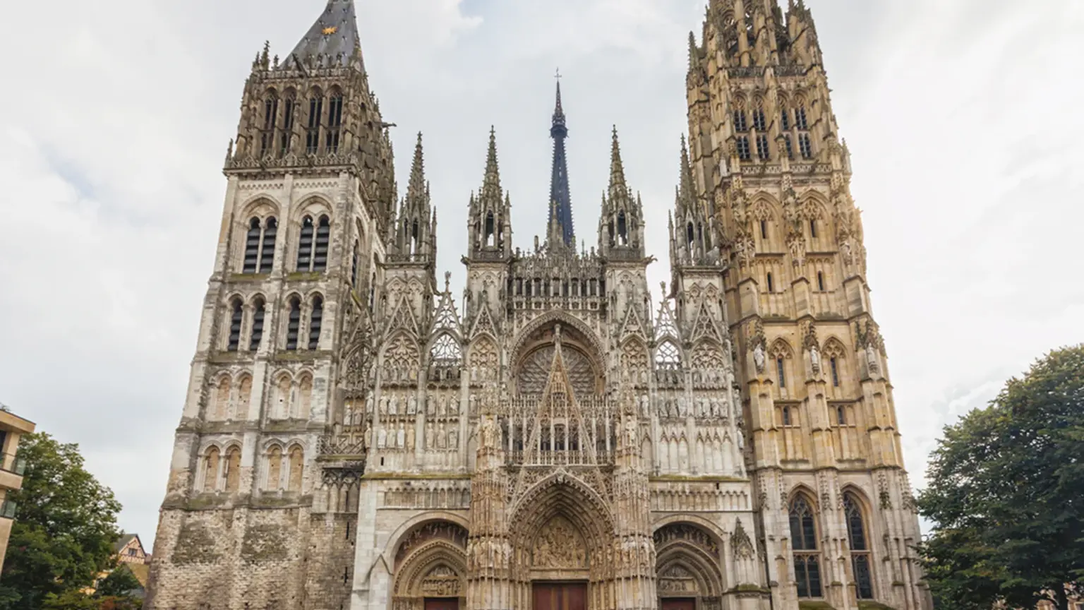 An ornate Gothic cathedral facade with two contrasting towers and a tall central spire on a wet square.