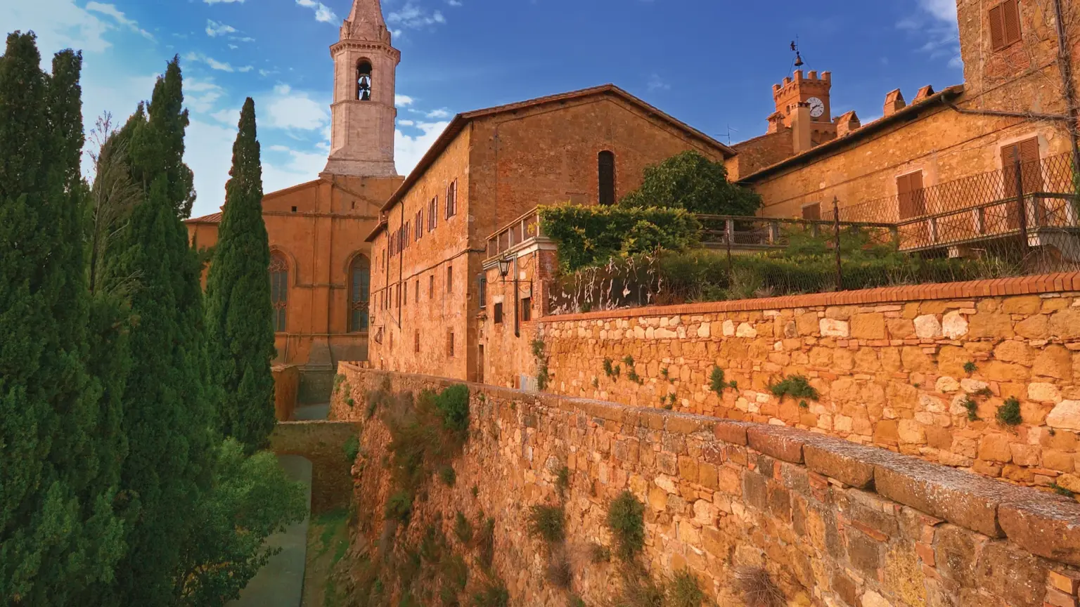 The honey-coloured stone buildings of Pienza with the cathedral bell tower, cypress trees in warm golden light