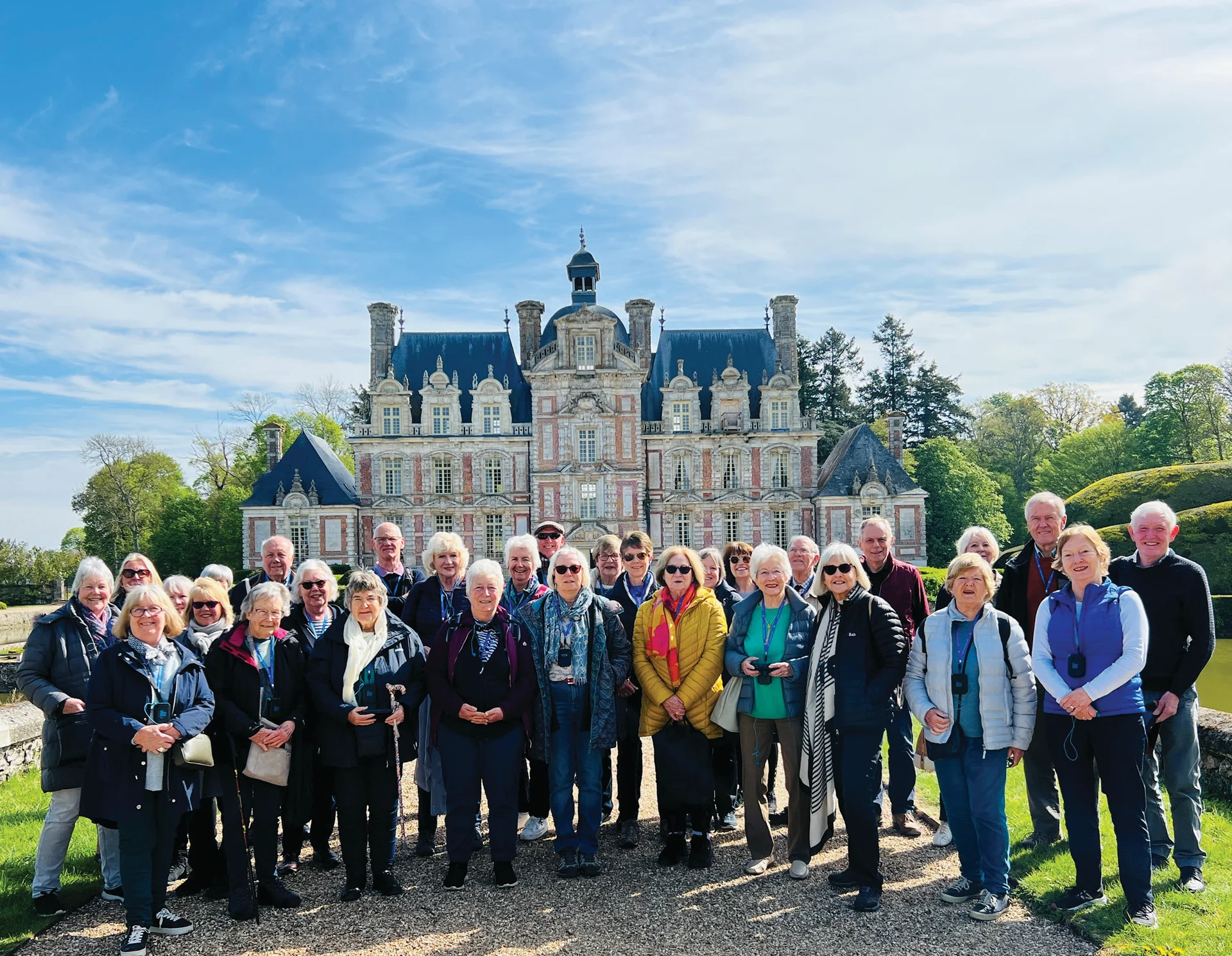 Group of visitors gathered outside Château de Beaumesnil, an ornate Baroque château surrounded by manicured grounds in Normandy.