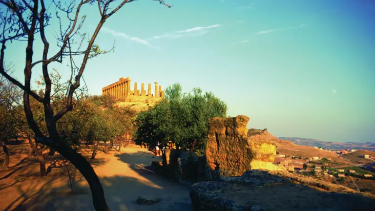 The Doric ruins of a Greek temple in the Valley of the Temples at Agrigento, golden columns standing against a blue Sicilian sky