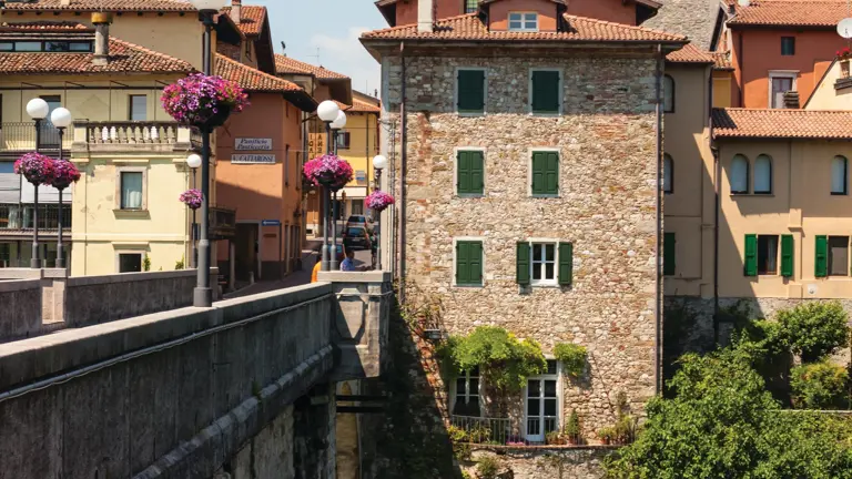 The stone Devil's Bridge with its two unequal arches crossing the turquoise Natisone river, medieval buildings on both banks