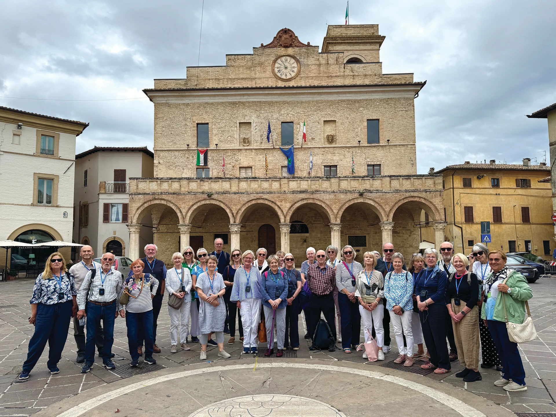 Group of visitors posed in the medieval hilltop town of Montefalco, with historic stone buildings and views across the countryside.