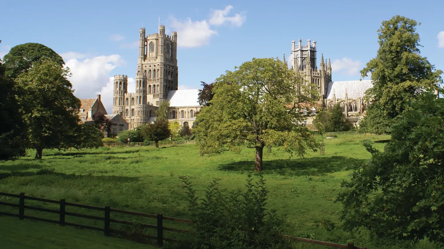 Medieval cathedral with central octagonal lantern tower and twin west towers, rising above a green close